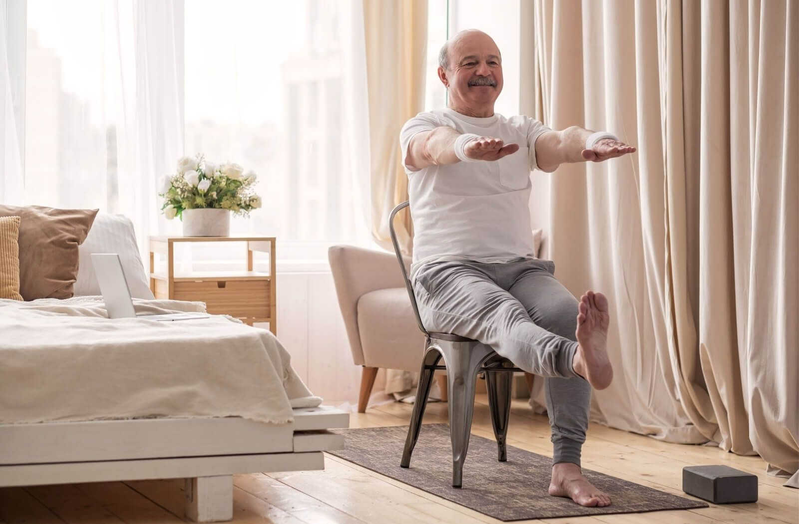 A senior man doing balance and stretching exercises on a chair at home.