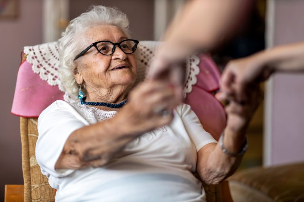 An older woman is smiling while holding hands with her caregiver.