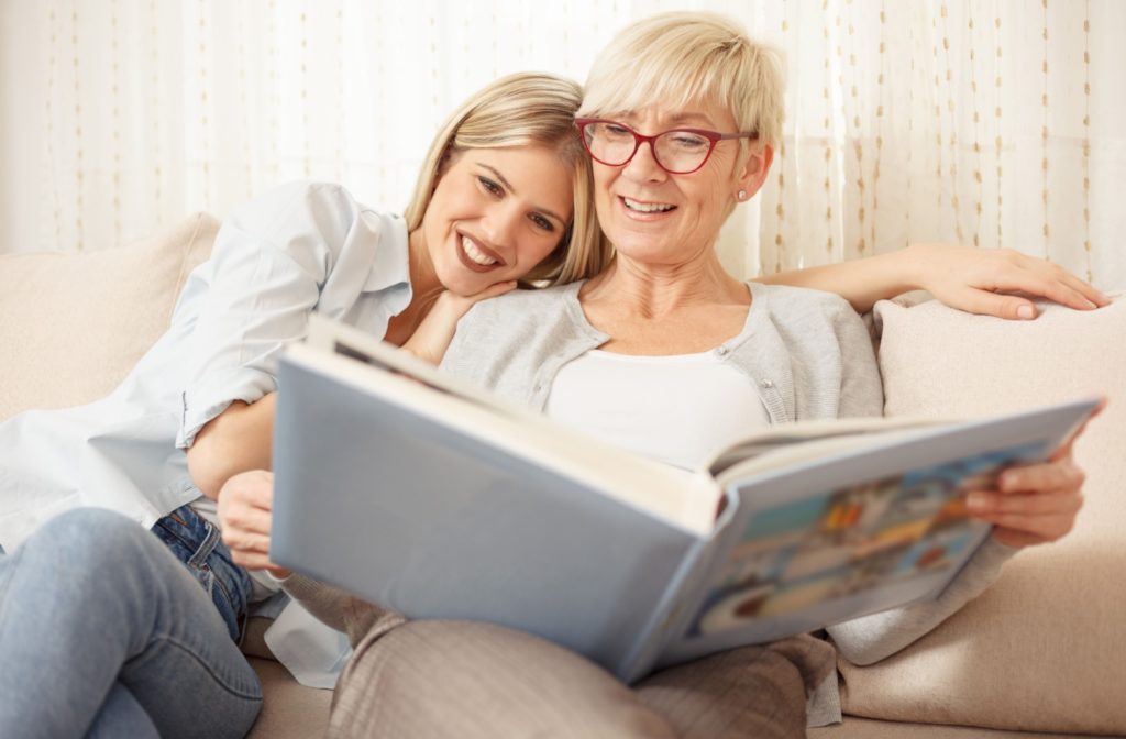 A mother and daughter sitting on a couch and happily reminiscing with old photos.