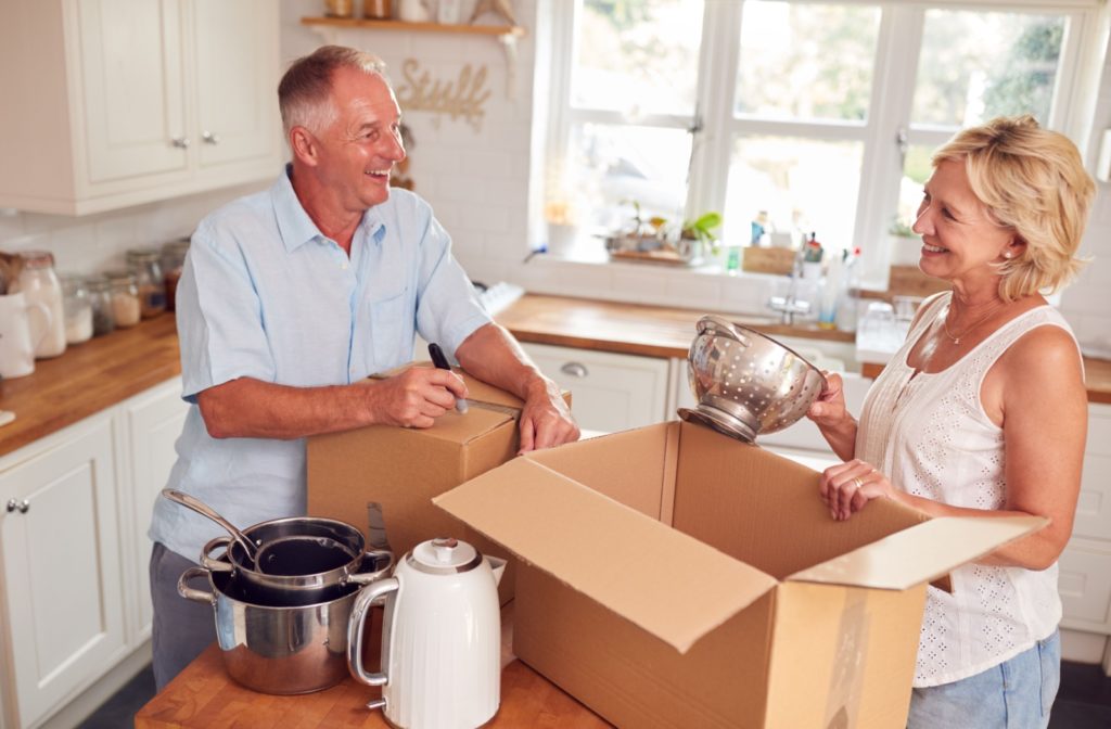 Senior Couple Downsizing In Retirement Packing And Labelling Boxes Ready For Move Into New Home.
