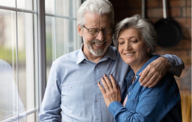 Happy senior couple hugging while standing next to each other at window