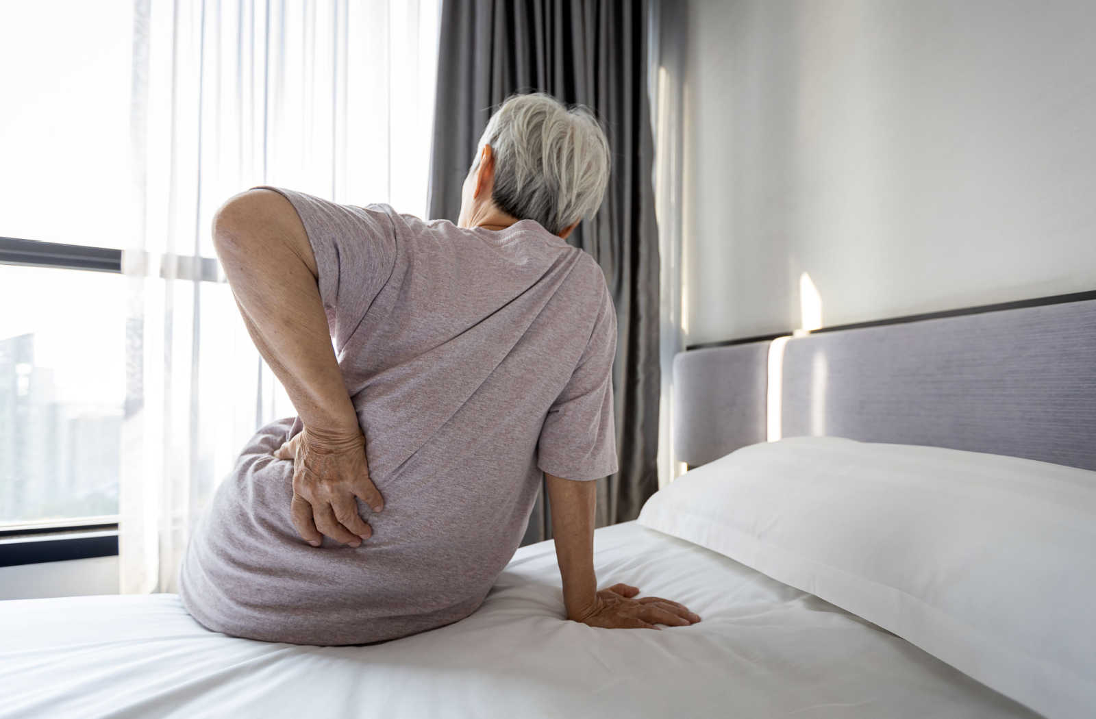 An older woman sitting on a bed with her hand on her hip