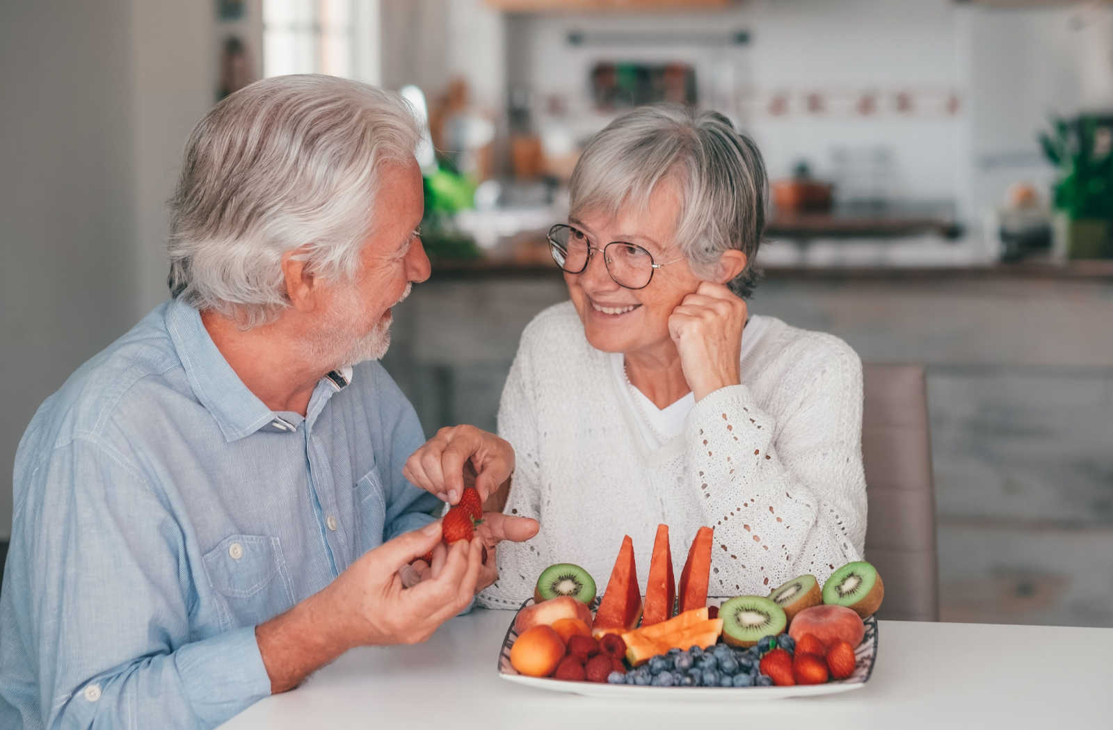 Senior couple sitting by the table eating fruits for snacks.