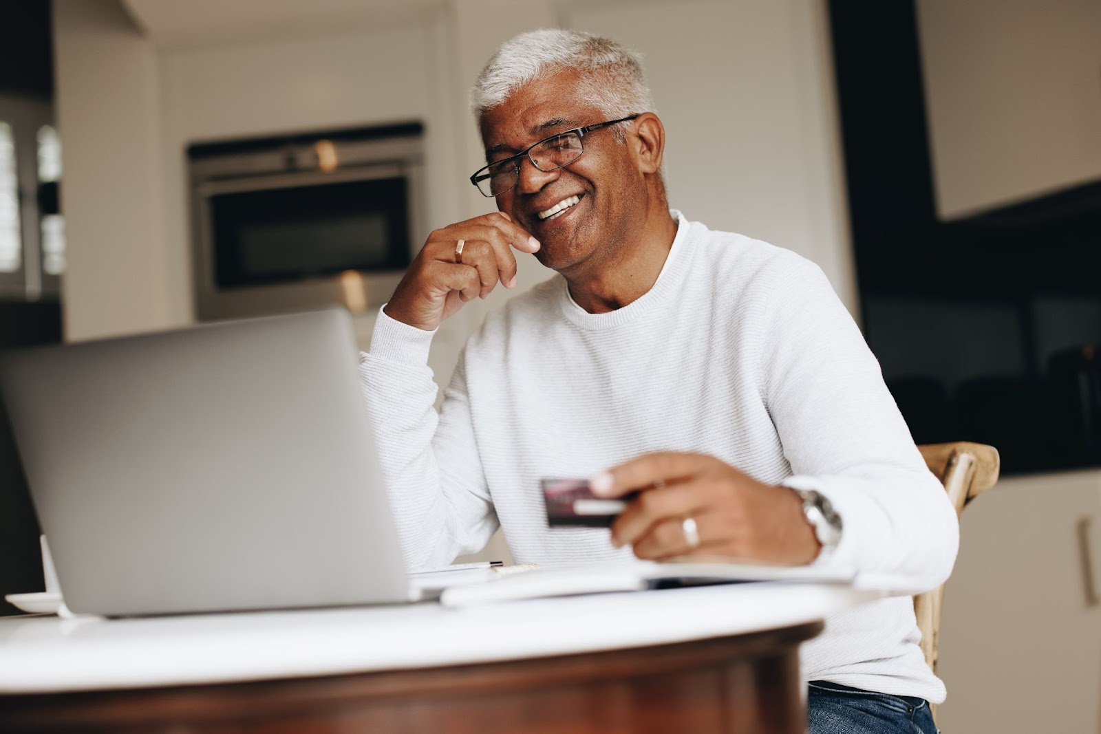 A smiling senior uses his laptop to order something online from the comfort of his home.