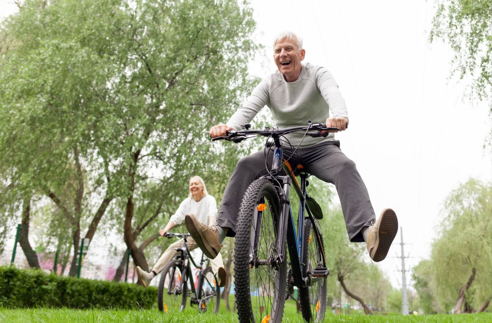 Two seniors riding bikes in a lush community park.
