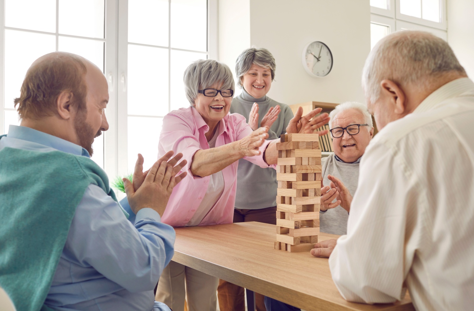 A group of older adults in senior living laughing together while stacking wooden blocks for a game.