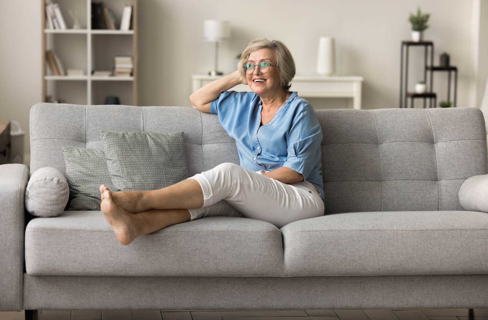Older woman relaxing on a sofa, smiling and looking comfortable in a living room.