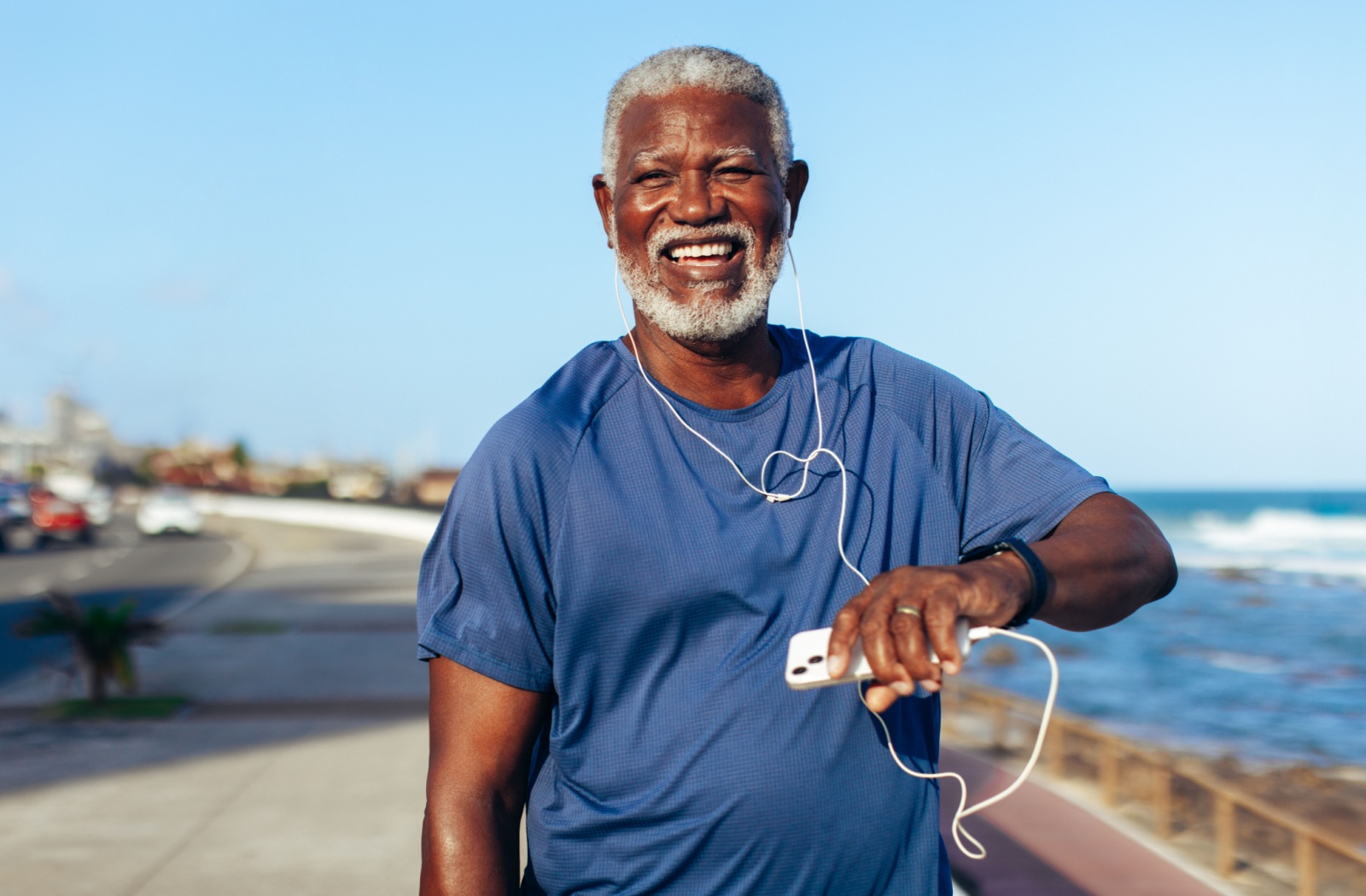 A happy senior listening to music on their phone looks at their watch while taking a break from a run to stay healthy.