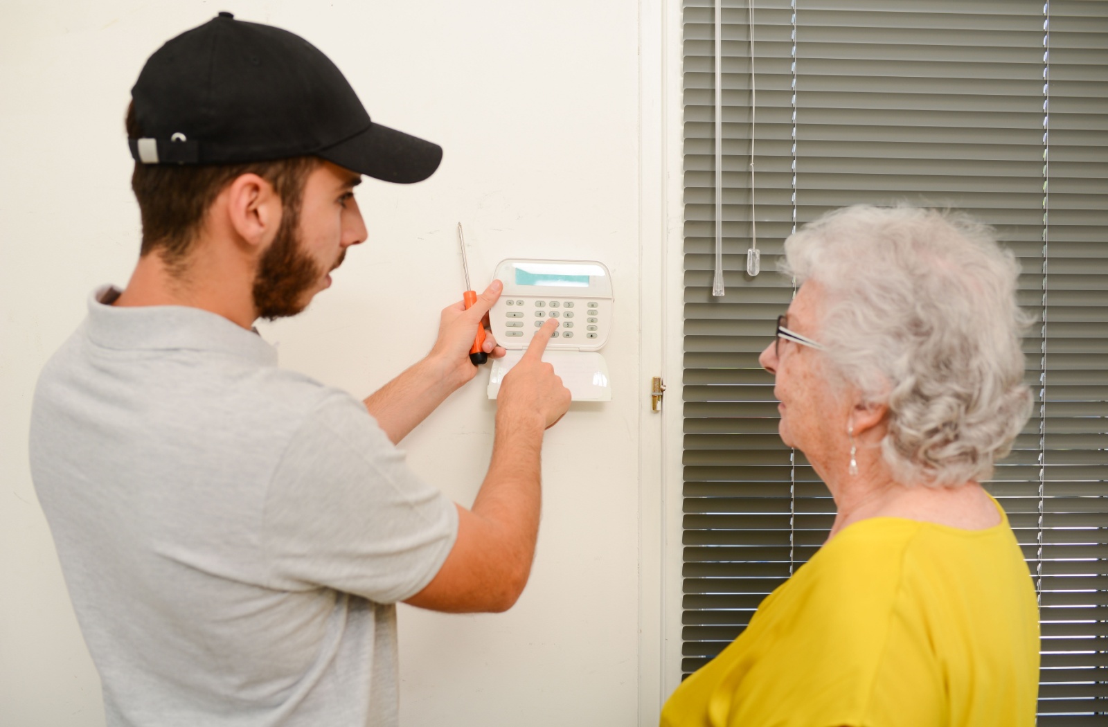 A home security expert shows a senior in yellow how to activate and deactivate their new home security system.
