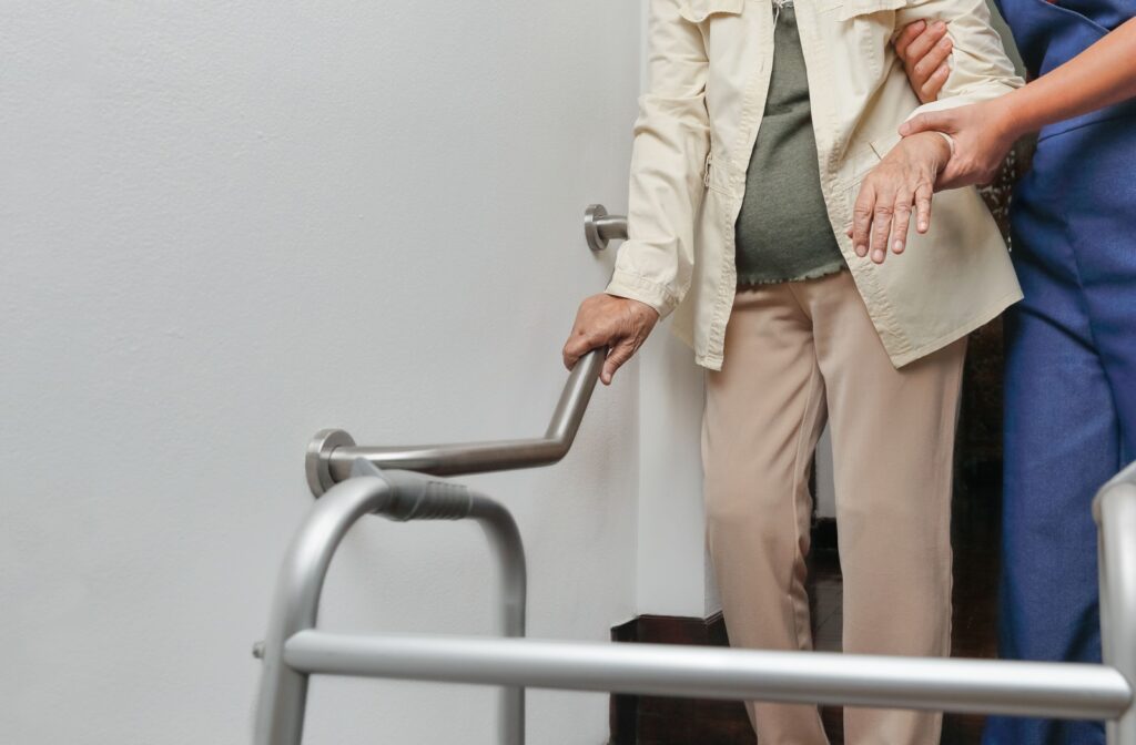 Along with the aid of a grab bar, a nurse helps a senior move through a bathroom back to their walker.