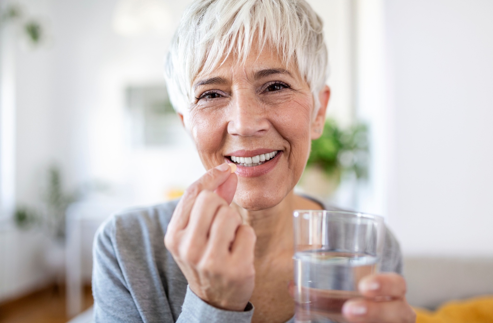 Senior woman smiling while taking a vitamin D supplement for bone health.