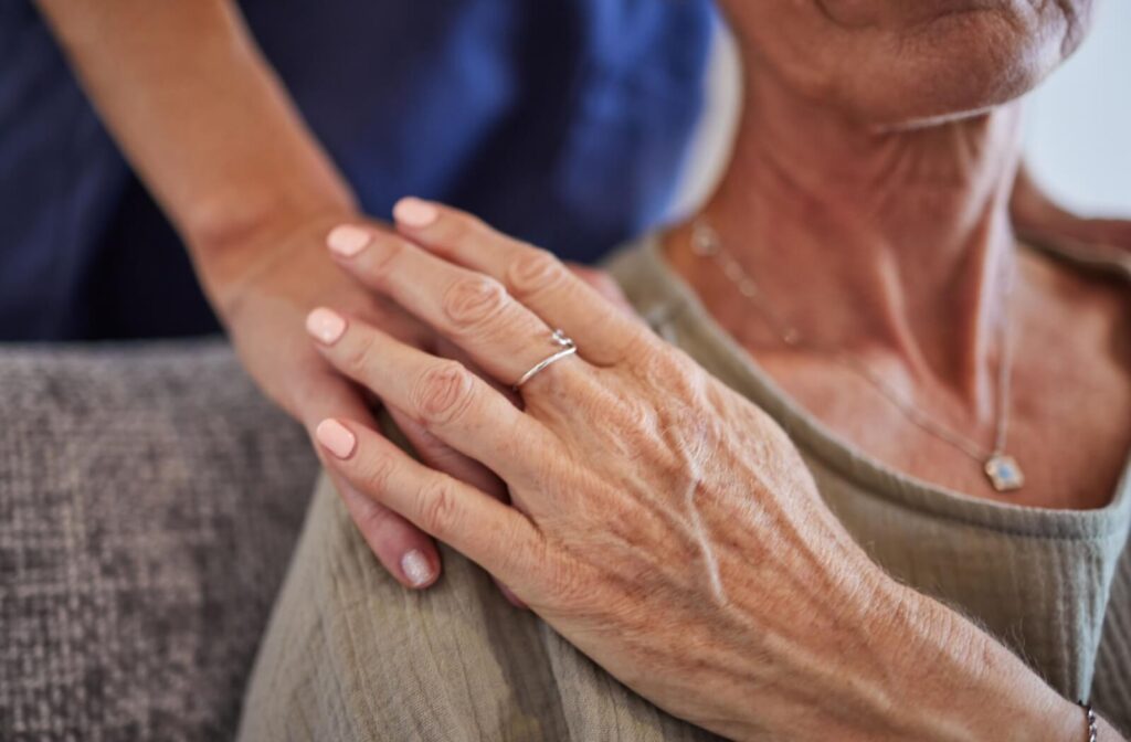 A close-up of a person standing behind a senior placing a reassuring hand on their shoulder in care and support