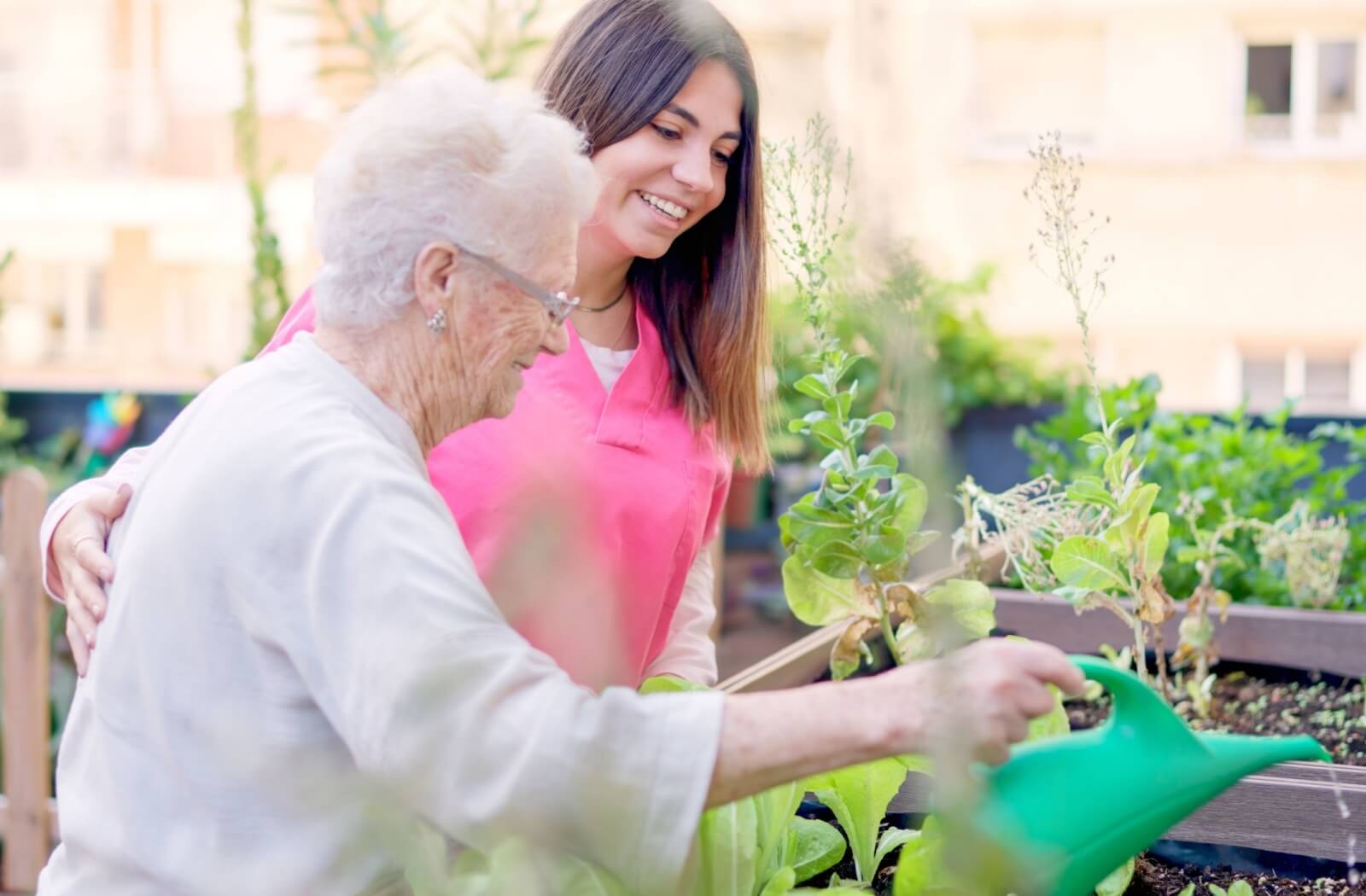A memory care team member assists a senior with watering the community garden.