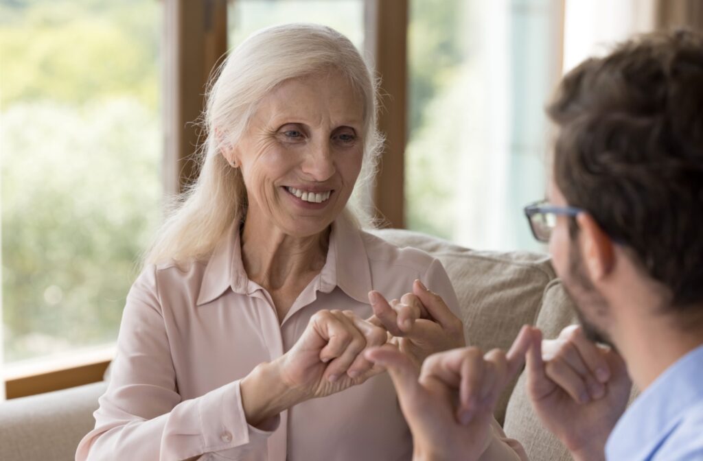 An older adult and a caregiver in senior living smiling while using sign language to communicate.