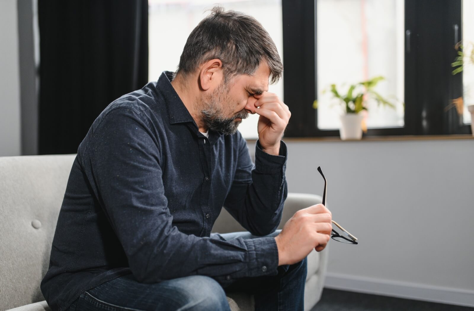A young adult sitting on their couch and rubbing the bridge of their nose due to caregiving stress and burnout.